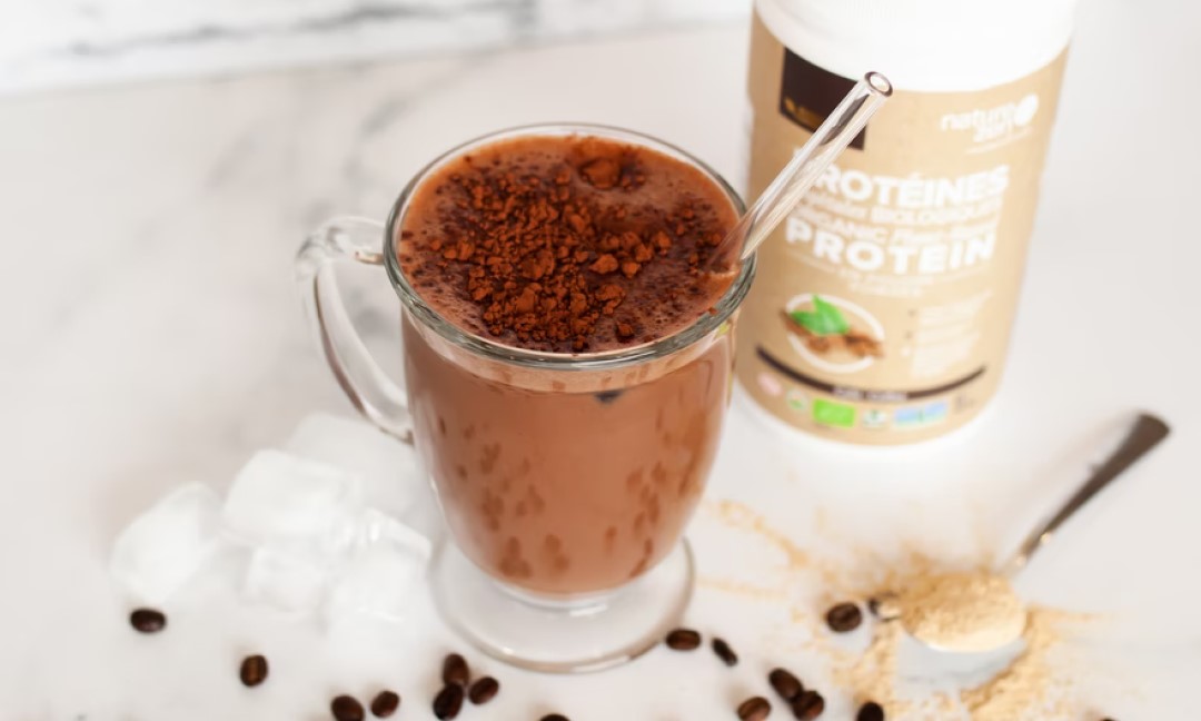 A glass full of a protein drink next to a container of protein powder.