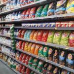 A store aisle with shelves full of packaged chips and other foodstuffs.